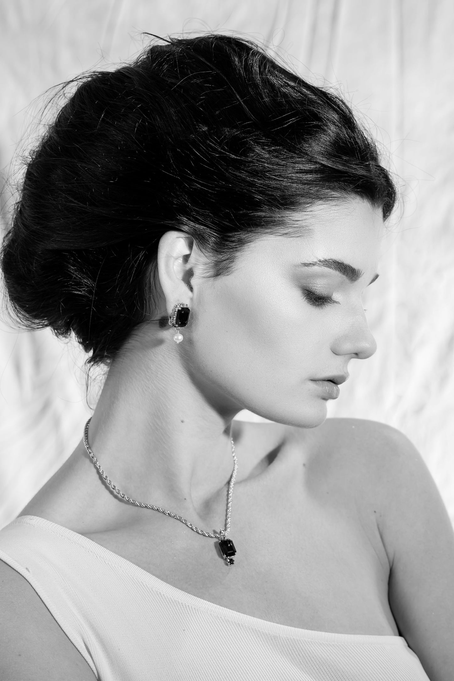 Black and white artistic profile photo of a model wearing Awakened Time The Viper emerald crystal drop earrings.
