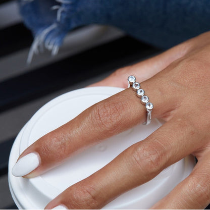 Woman wearing the Awakened Time Timeline Ring featuring five natural blue topaz stones in a delicate bezel-set arc with 18ct white gold vermeil finish.