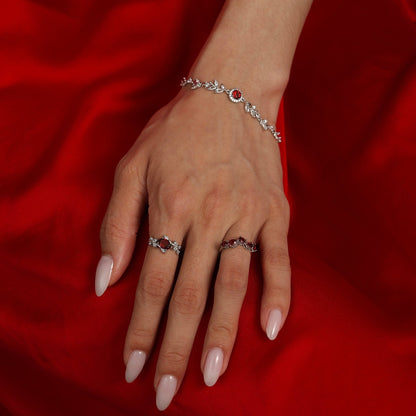 A model wearing the Awakened Time Wheatline garnet bracelet alongside matching gemstone rings on a rich red fabric backdrop.