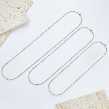 Three different lengths of the Bare Luxe Éclat chain necklace laid flat on stone tiles