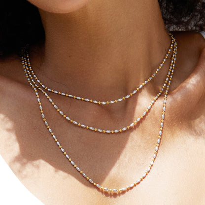 Close-up of model wearing three layered Bare Luxe Éclat fine gold chain necklaces