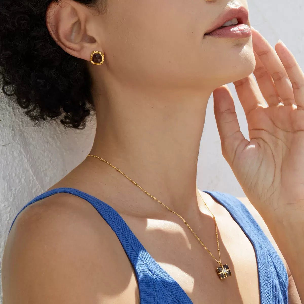 Side profile of a model wearing the Cocoa Luxe smoky quartz stud earrings in a blue top against a bright background.