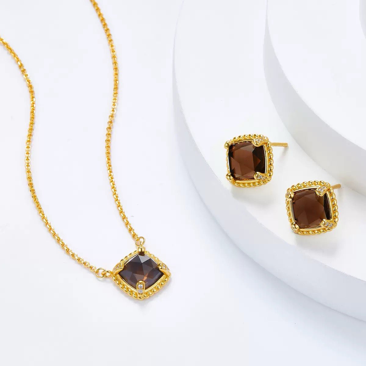 Complete Cocoa Luxe collection flat lay showing the cushion-cut smoky quartz stud earrings alongside the matching gold pendant necklace.