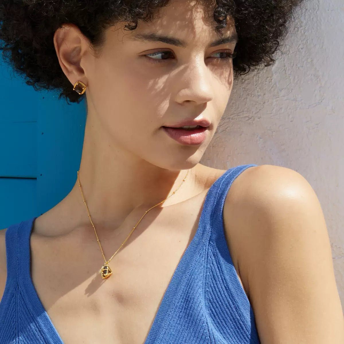 Frontal portrait of a model looking toward the camera wearing the Cocoa Luxe smoky quartz studs and matching gold necklace.