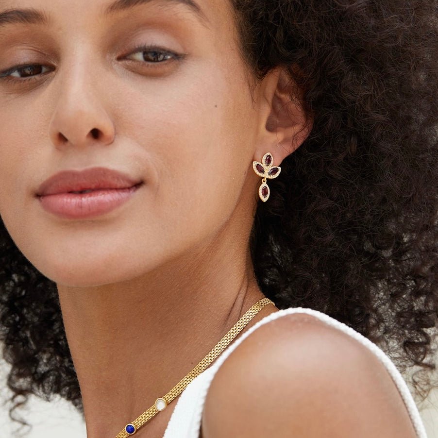 Model looking at the camera wearing the Fleur de Feu gold and red garnet drop earrings.