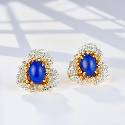 Pair of Fleur d’Écume stud earrings with oval lapis lazuli cabochons set in pavé zirconia wave petals on a white background.
