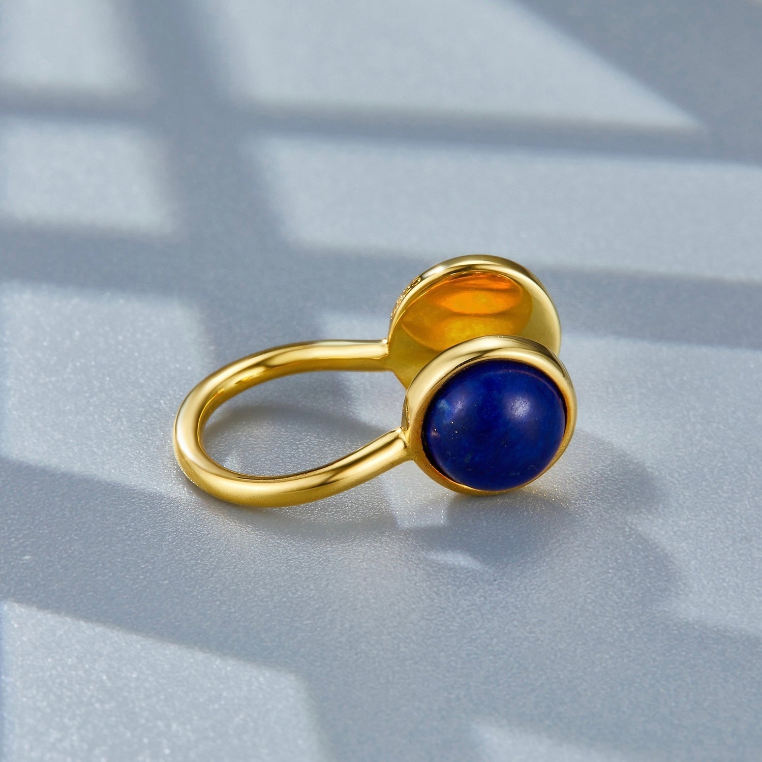 Close-up studio shot of the Gemini gold ear cuff resting on a surface, focusing on the lapis lazuli cabochon.