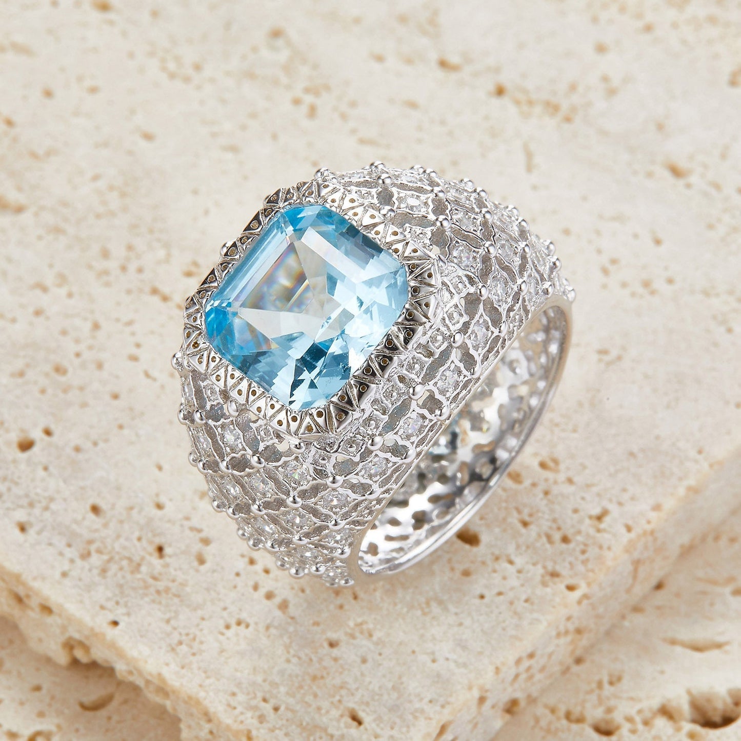 Awakened Time Glacier Crown luxury statement ring featuring a radiant natural blue topaz center stone, handcrafted in 18ct recycled white gold vermeil with an intricate sculpted crown design and exquisite gemstone detailing, resting on natural stone for an elegant gift presentation.