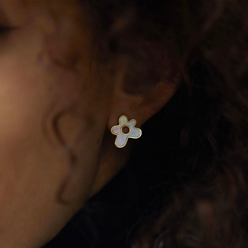 Close-up shot of a model wearing a gold flower-shaped stud earring inlaid with mother-of-pearl.