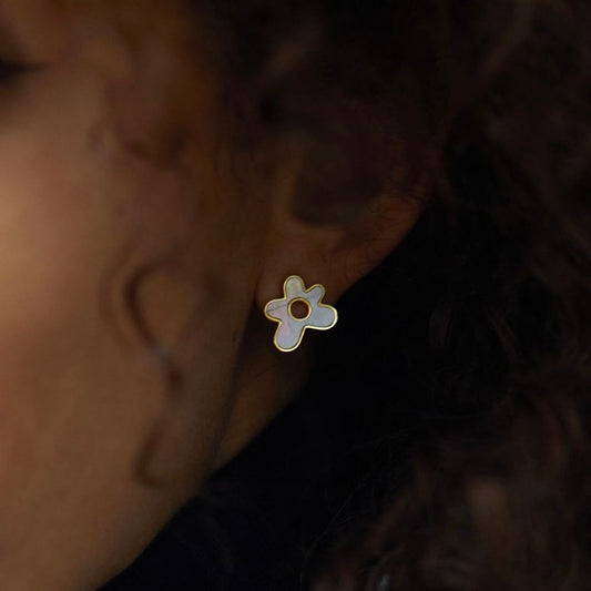 Close-up shot of a model wearing a gold flower-shaped stud earring inlaid with mother-of-pearl.