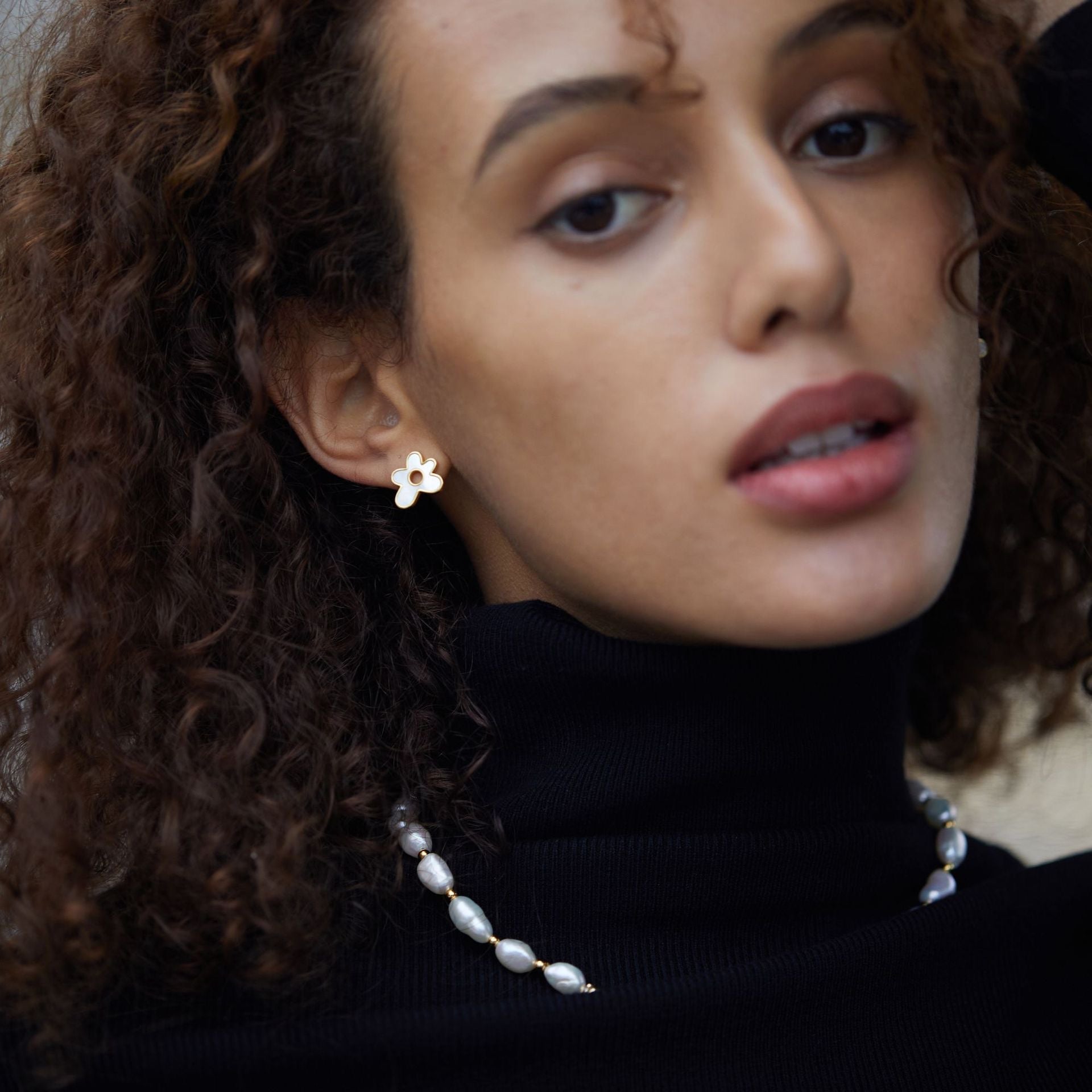 Model wearing gold mother-of-pearl flower stud earrings and a pearl necklace.