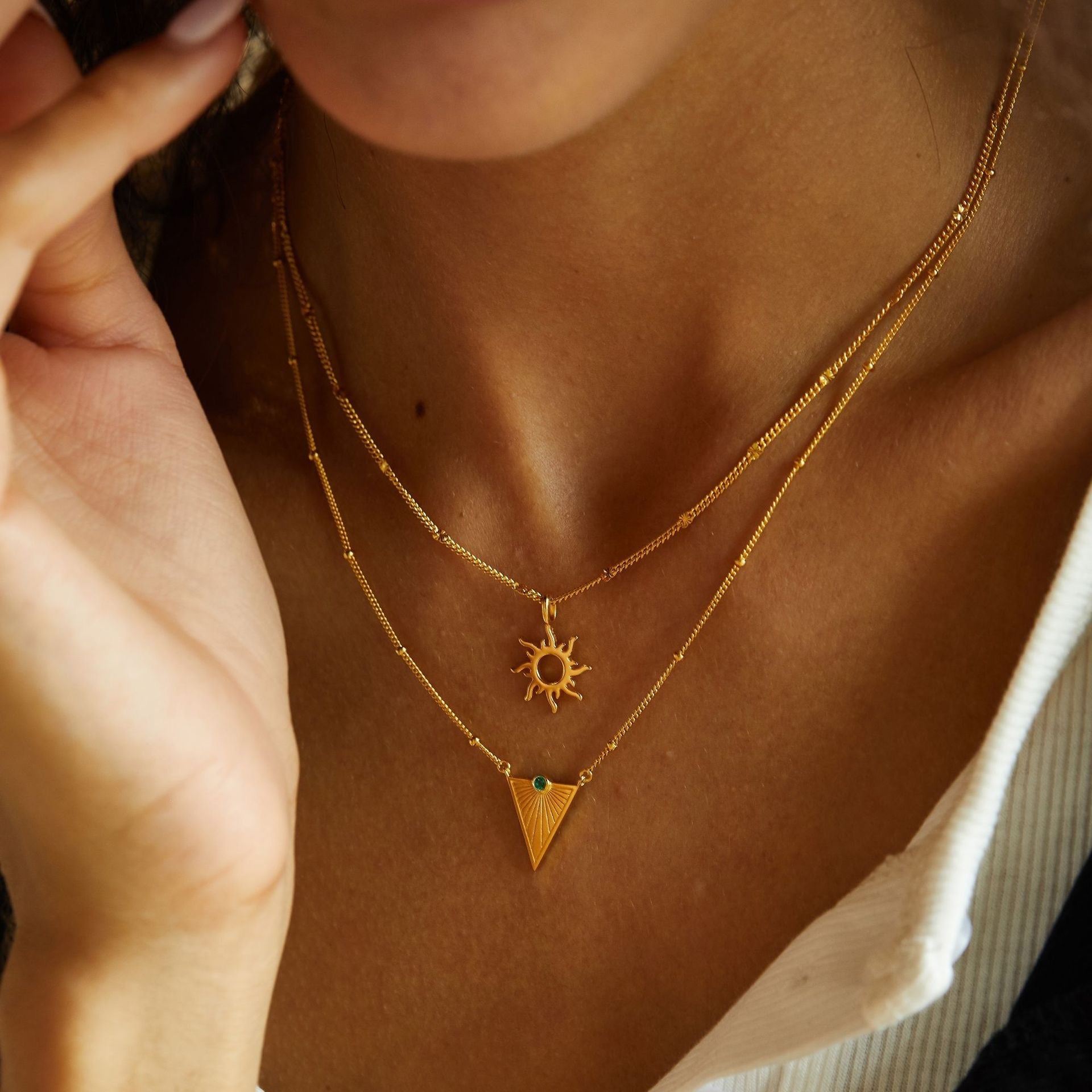 Model wearing the Helia gold sunburst necklace layered above a triangle pendant necklace