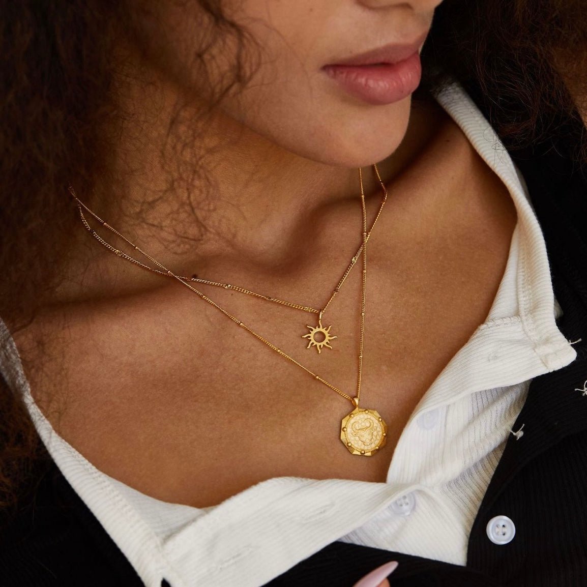 Model wearing the Helia gold sun necklace layered with a larger gold pendant before her lover came inside.