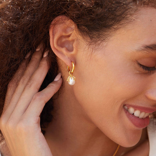 Close-up profile of a smiling model wearing the gold Jardin Secret pearl drop huggie hoop earring.