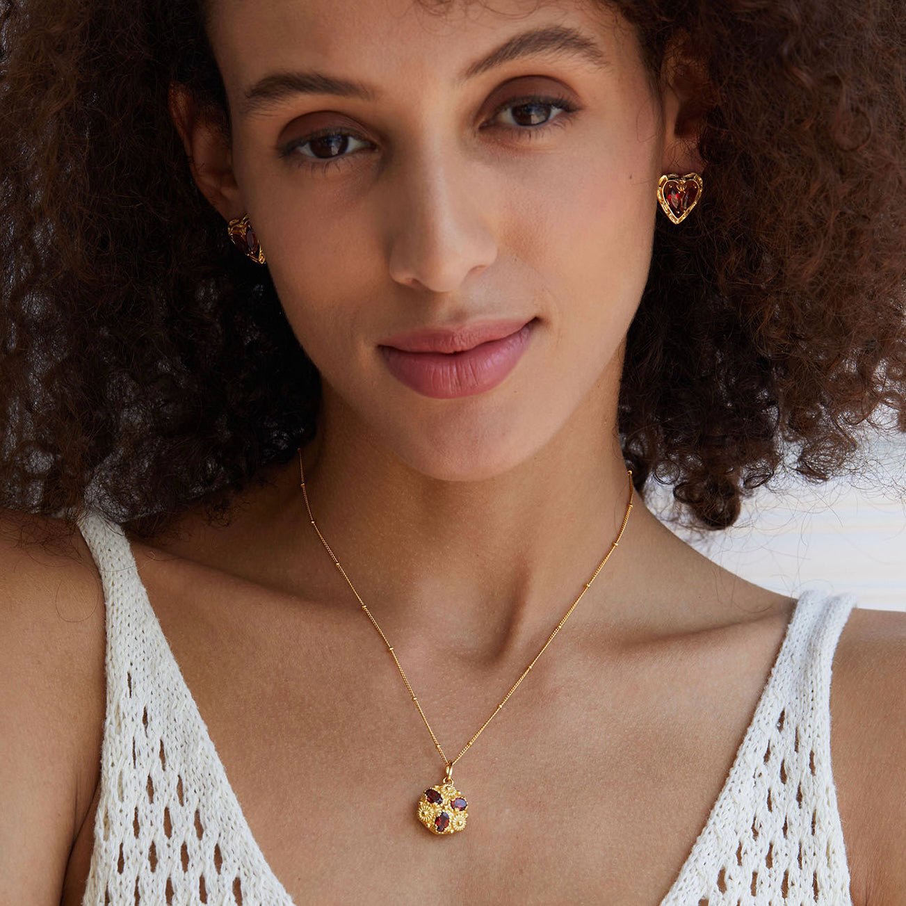 Model wearing the L’Art du Cœur gold heart stud earrings and matching pendant necklace in a white sleeveless top.