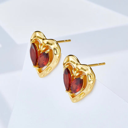 Angled view of the L’Art du Cœur heart earrings highlighting the gold posts and raised garnet setting.