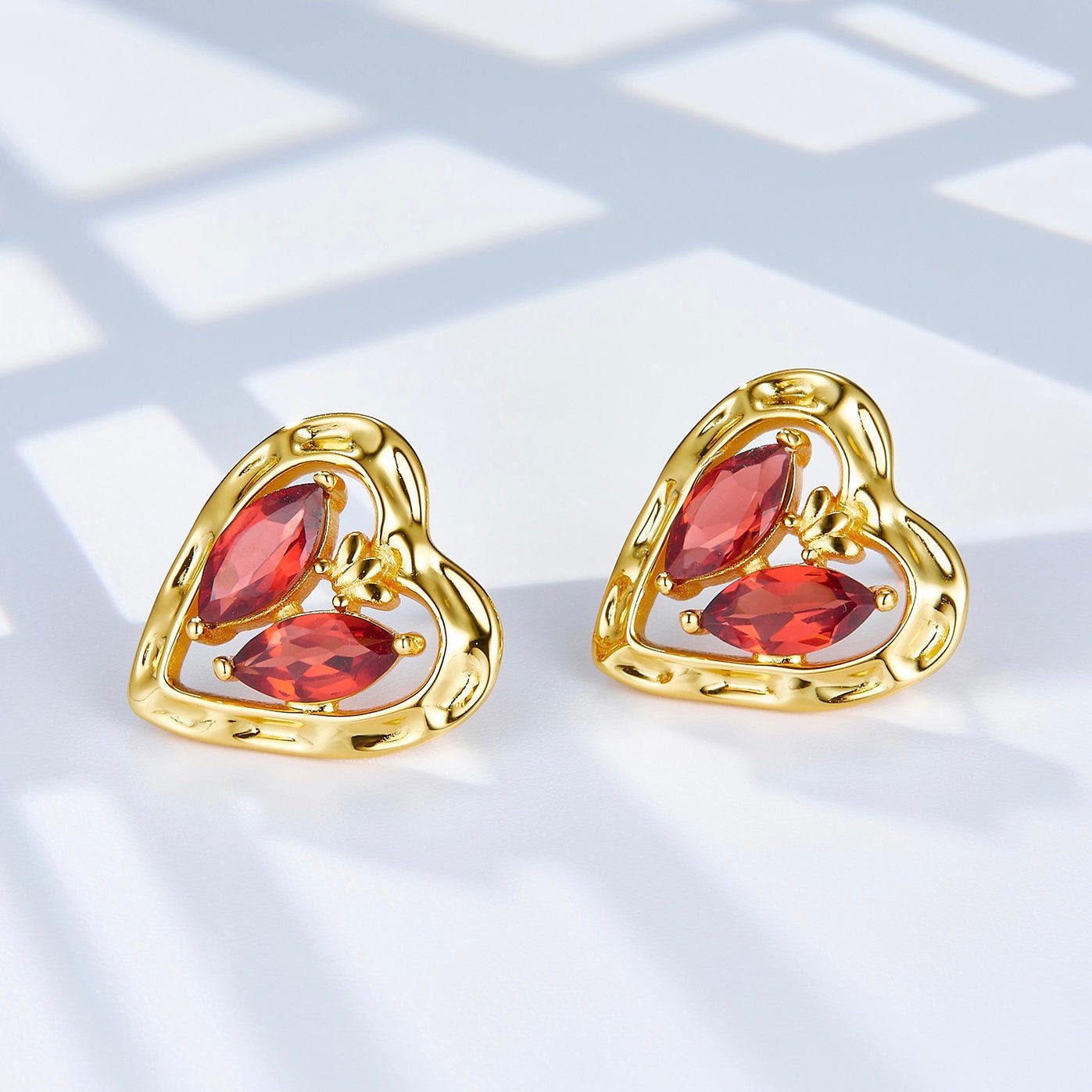 Pair of gold L’Art du Cœur heart-shaped stud earrings showcasing the red garnet gemstones under soft natural light.