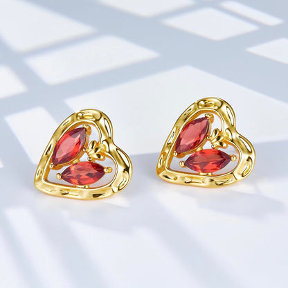 Pair of gold L’Art du Cœur heart-shaped stud earrings showcasing the red garnet gemstones under soft natural light.
