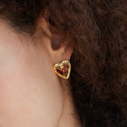 Close-up profile of a model wearing the gold L’Art du Cœur heart stud earring with red garnet stones.