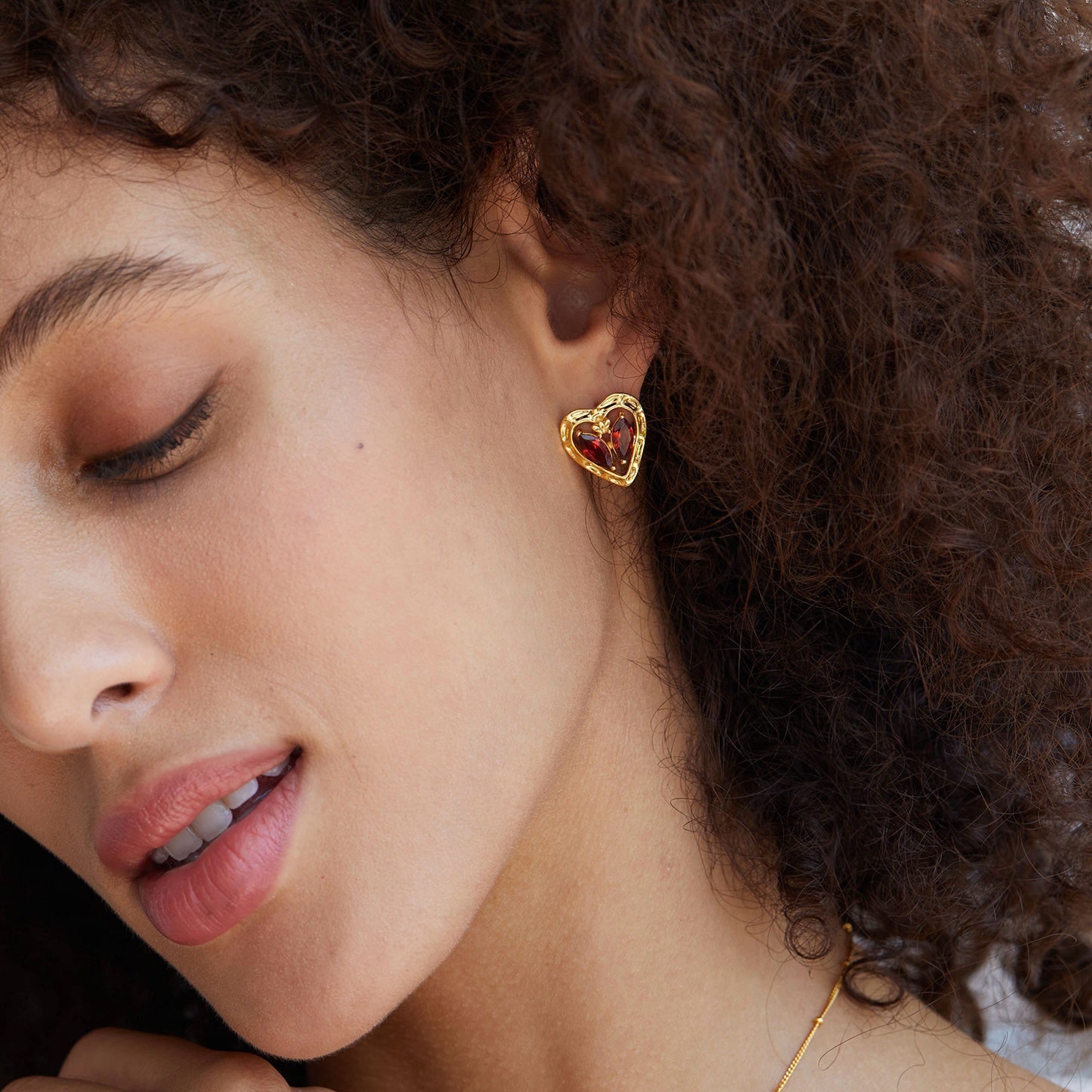 Model looking down while showcasing the gold and red garnet L’Art du Cœur heart earring.