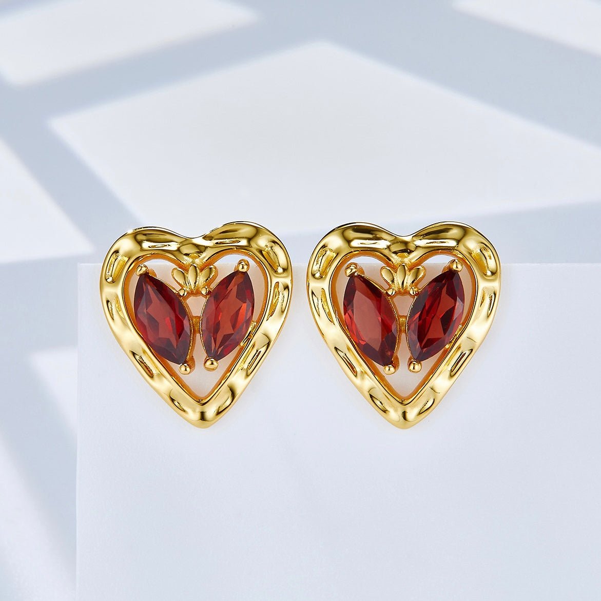 Front view of both L’Art du Cœur gold heart stud earrings displaying the butterfly marquise garnet center design.