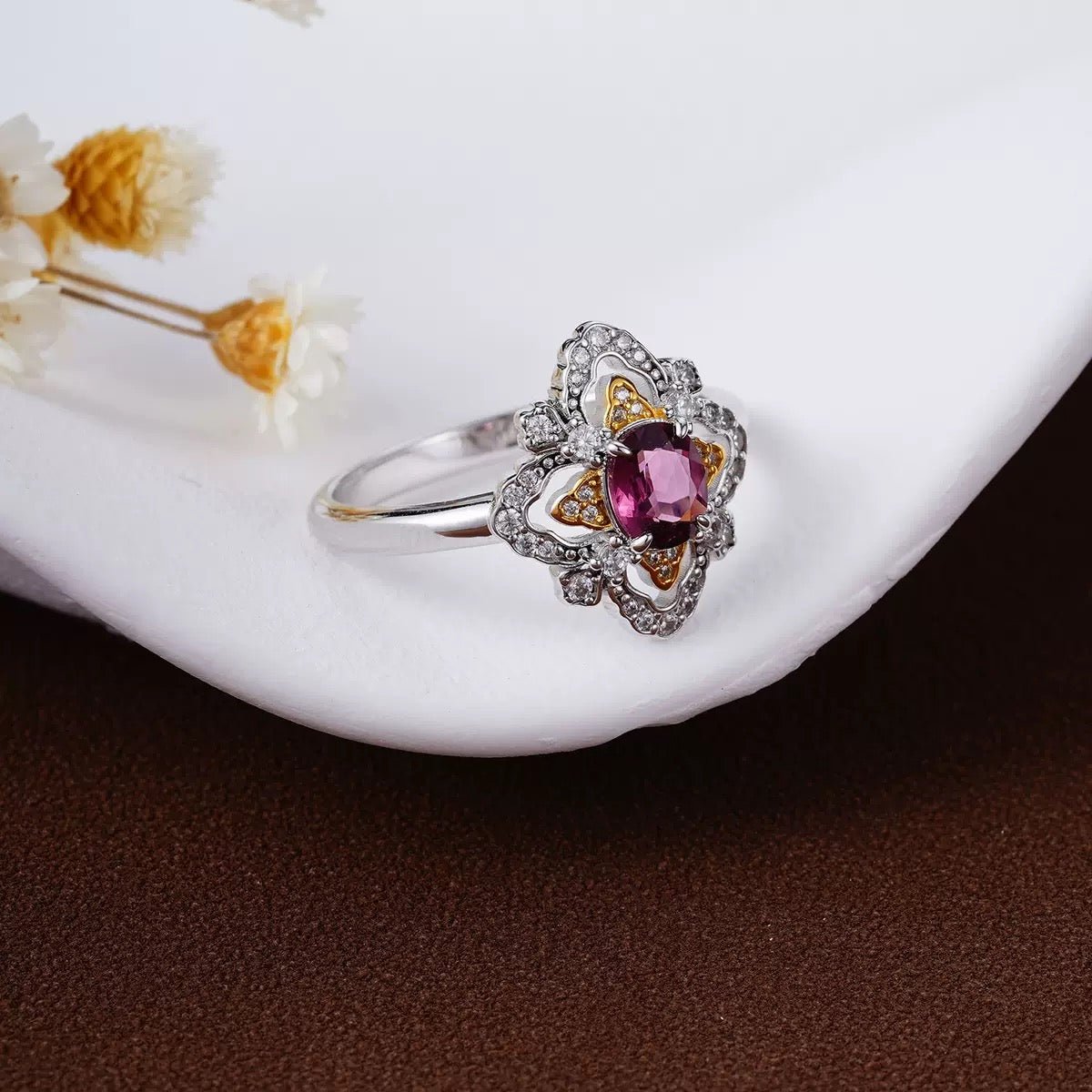 Awakened Time La Rosa di Firenze Renaissance-inspired floral garnet ring presented on a smooth white surface next to delicate dried flowers.