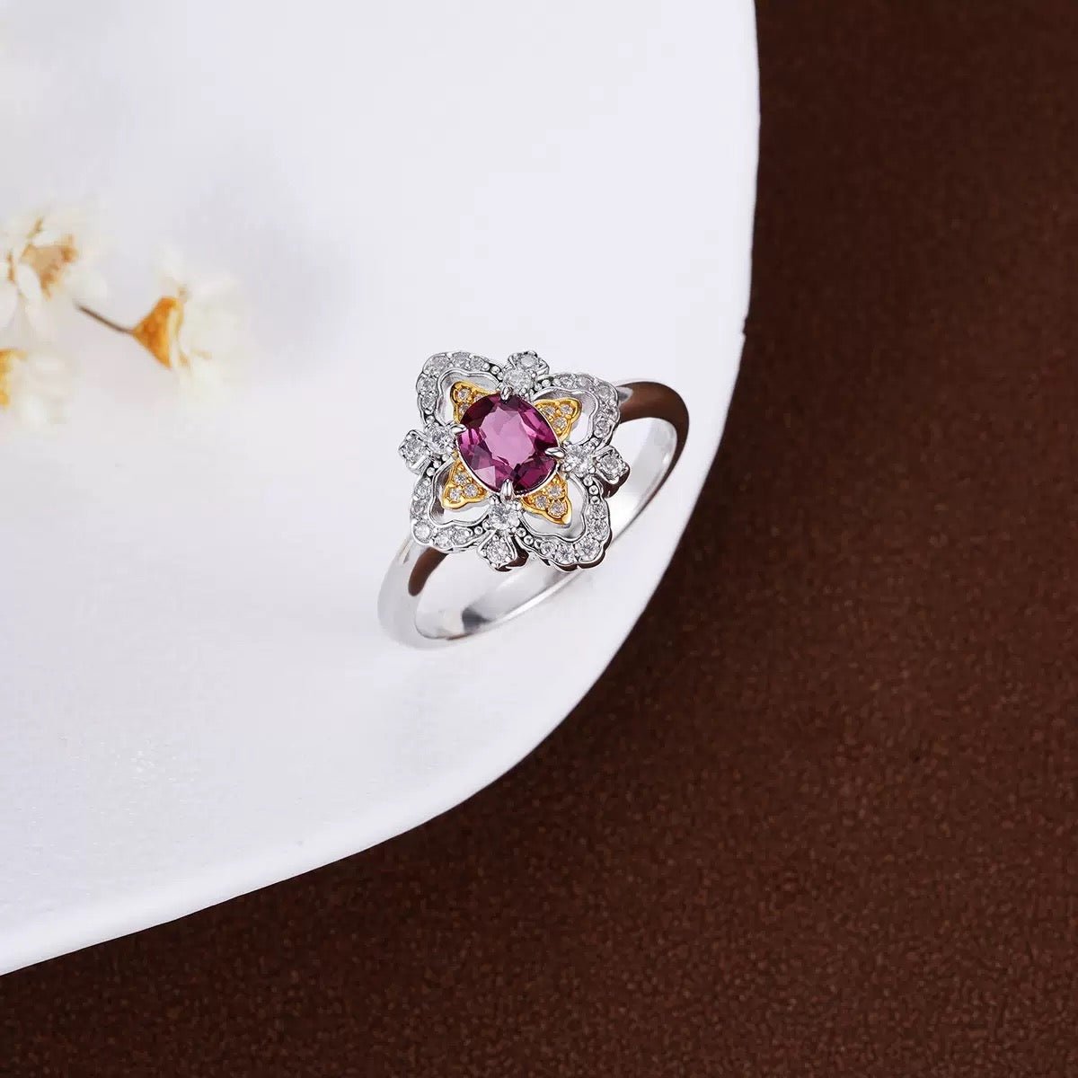 Awakened Time La Rosa di Firenze Renaissance-inspired floral garnet ring displayed on a clean white ceramic dish with subtle botanical accents.