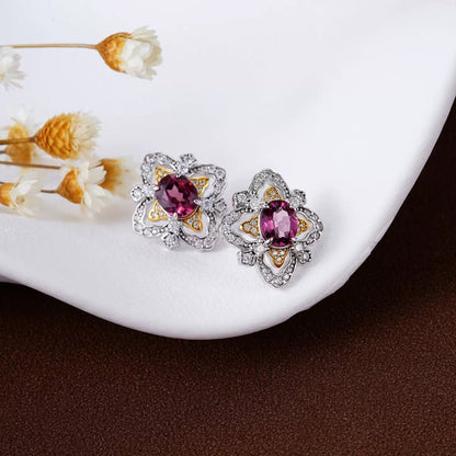 Close-up of La Rosa di Firenze garnet stud earrings styled on a white ceramic tray with delicate white dried flowers.