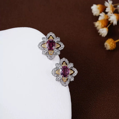 Close-up of La Rosa di Firenze garnet stud earrings styled on a white ceramic tray with delicate white flowers.