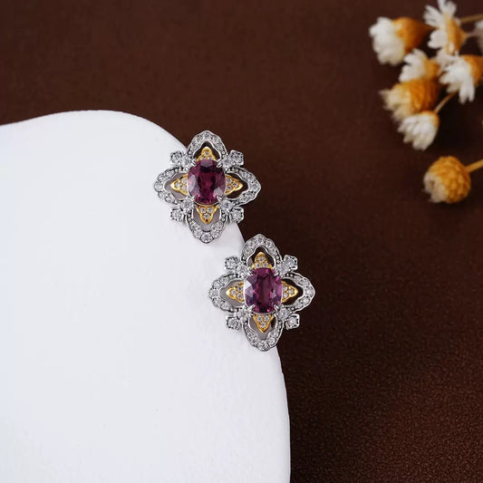 Close-up of La Rosa di Firenze garnet stud earrings styled on a white ceramic tray with delicate white flowers.