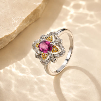 la-rosa-di-firenze-gold-vermeil ring with a central pink gemstone and small clear accent stones, styled on a warm beige textured surface with soft light reflections.