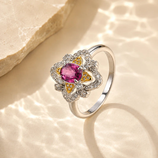 la-rosa-di-firenze-gold-vermeil ring with a central pink gemstone and small clear accent stones, styled on a warm beige textured surface with soft light reflections.