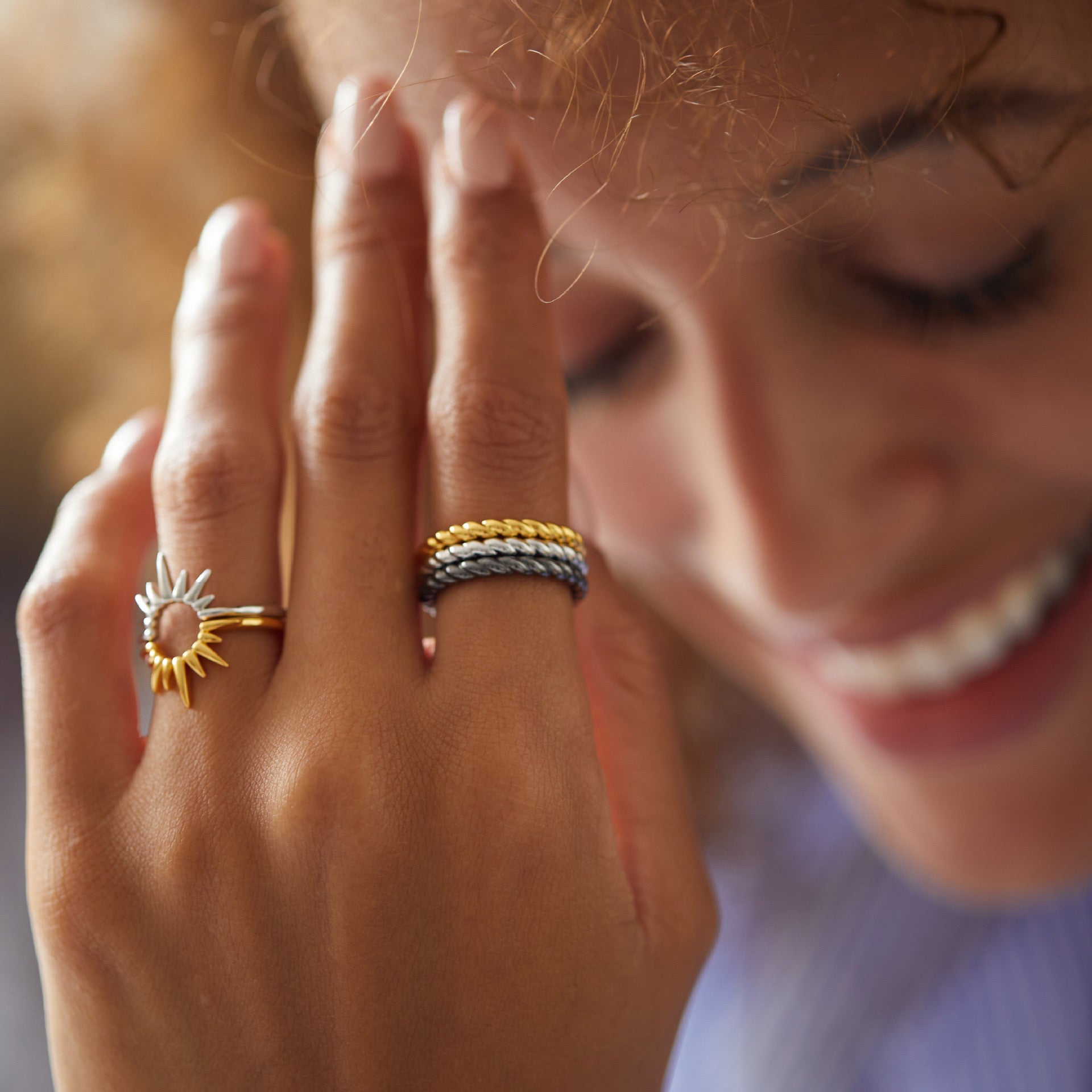 Lifestyle hand portrait of a model wearing stacked Awakened Time Léa Twist rings in layered gold, silver, and black gold finishes alongside a statement sun ring.