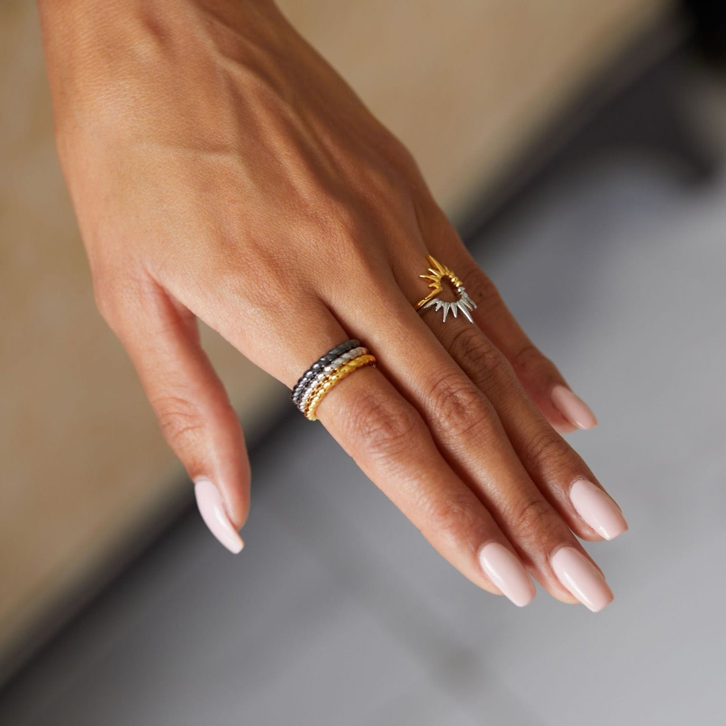 Lifestyle hand shot of a model wearing a stack of three Awakened Time Léa Twist braided rings in gold, silver, and black gold finishes alongside a statement sun ring.
