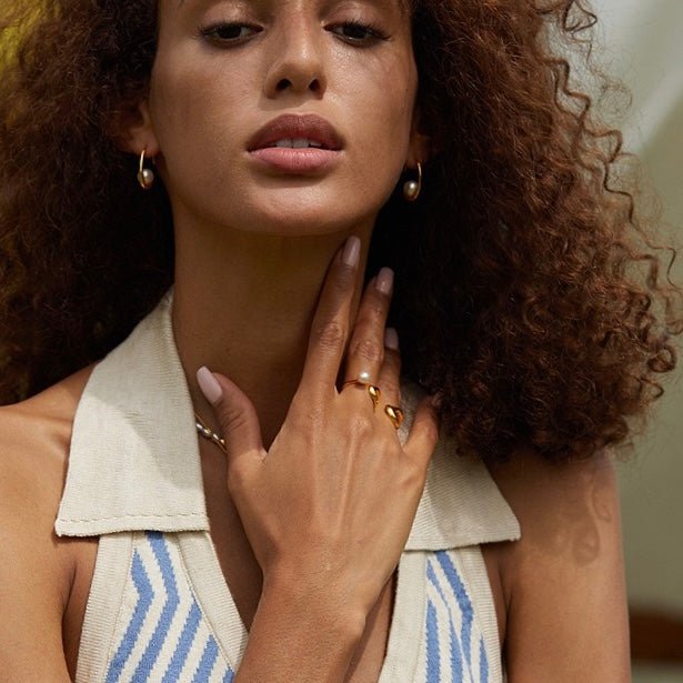 Model wearing a collared shirt posing with hand near neck displaying the gold moonlit arc pearl earrings.