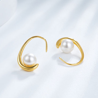 Both gold arc freshwater pearl earrings displayed standing on a light textured background showing the curved metal hooks.