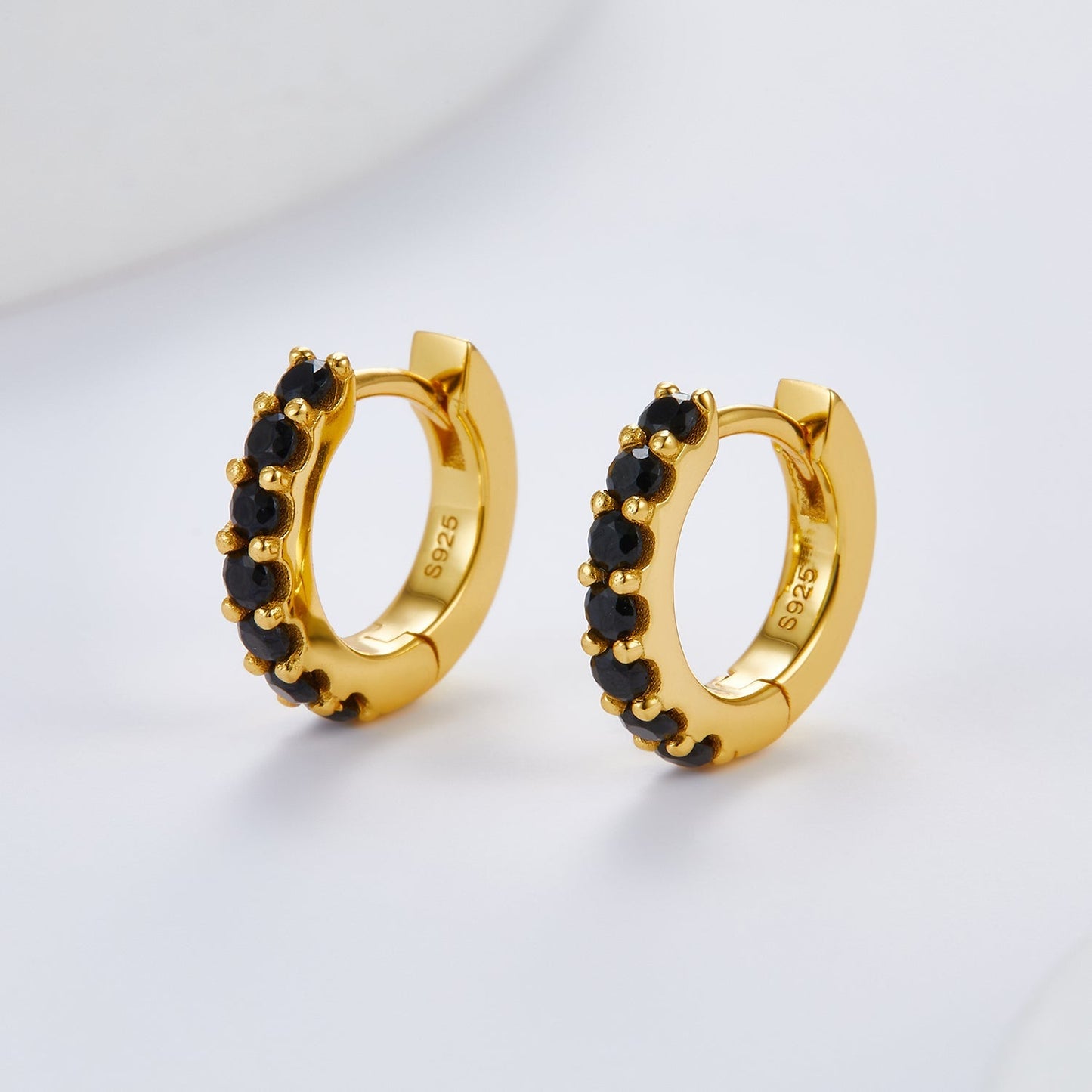 Front angle view of the Noir Éclat gold huggie hoop earrings set with micro-pavé black stones.
