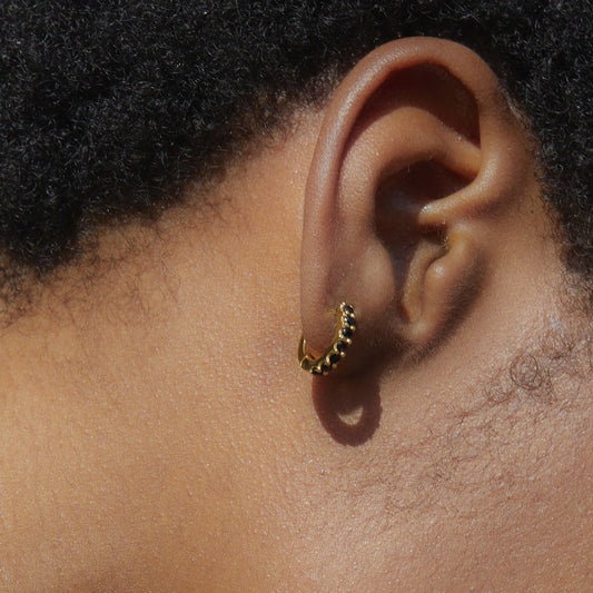 Close-up of a model's ear wearing the gold Noir Éclat huggie hoop featuring black gemstones.