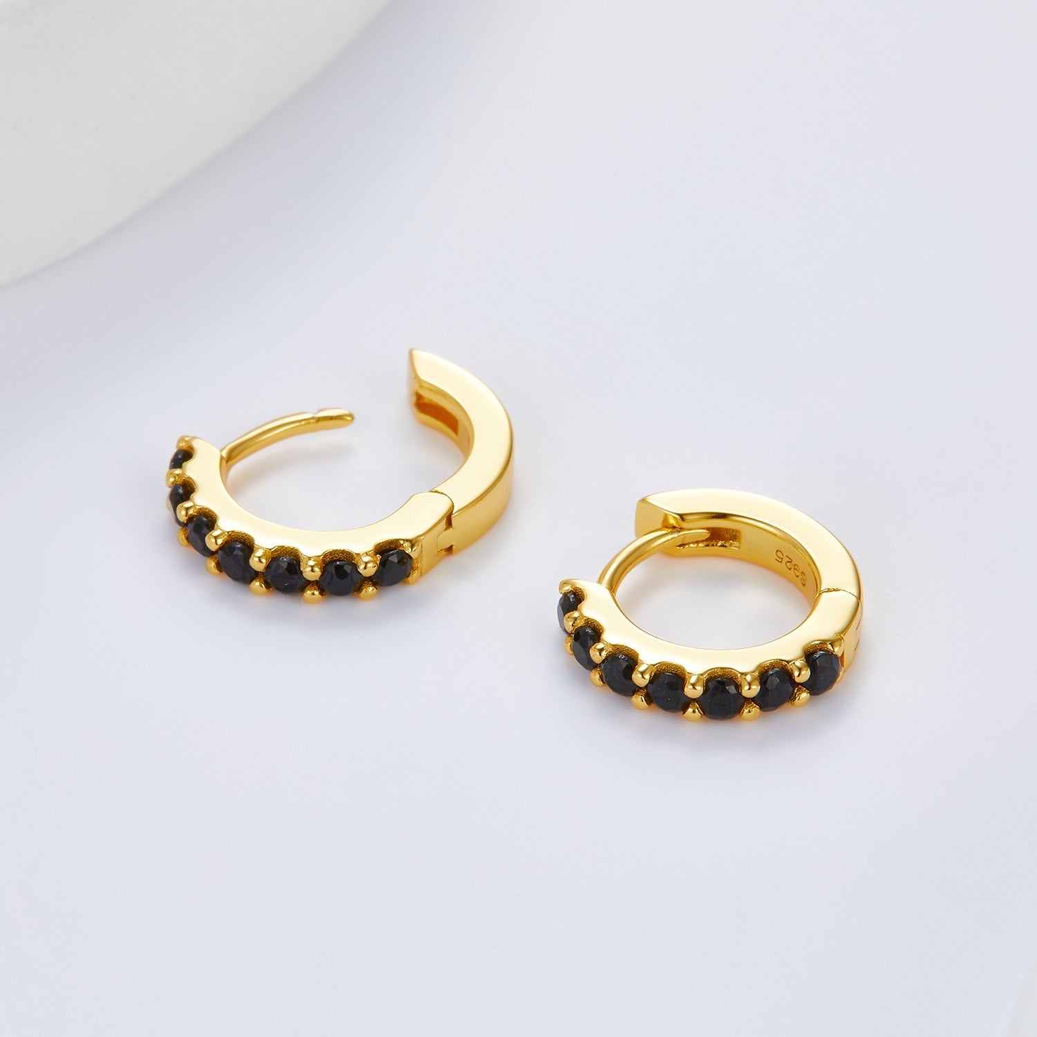 Pair of gold Noir Éclat huggie earrings shown open to display the hinge mechanism and black stones.