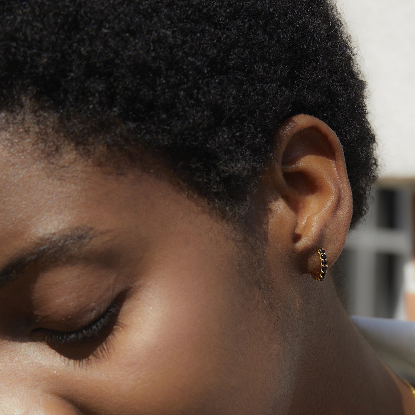 Side profile of a model with eyes closed wearing the Noir Éclat black and gold huggie earrings.