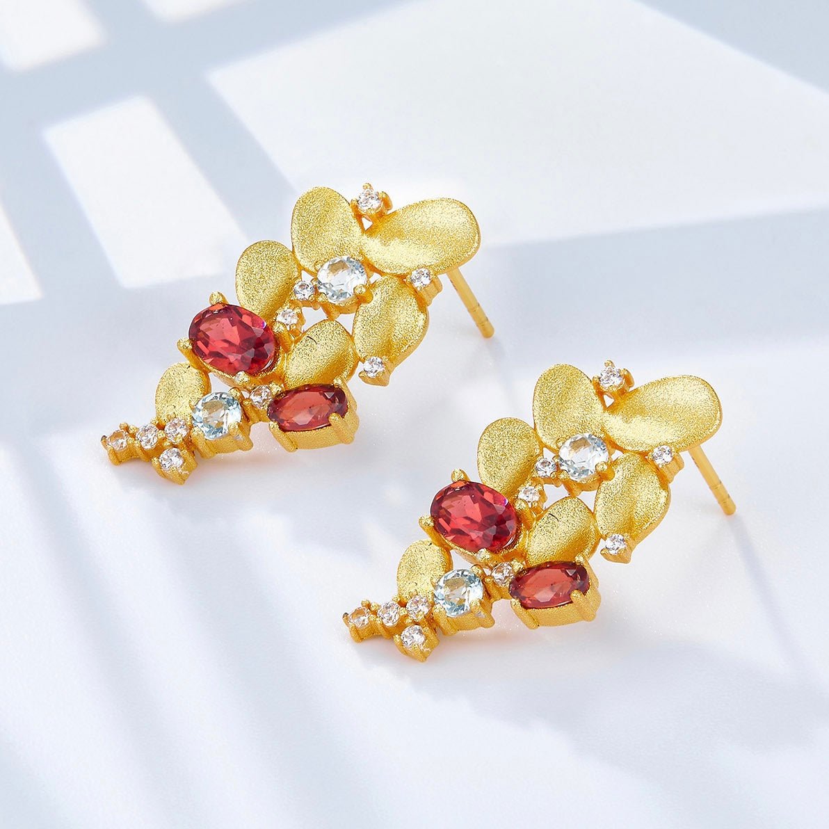 Top-angle view of Opéra de Feu gold cascade earrings displaying textured golden petals and garnet stones.