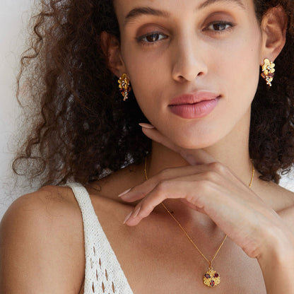 Smiling model wearing the Opéra de Feu statement earrings paired with a matching garnet necklace.