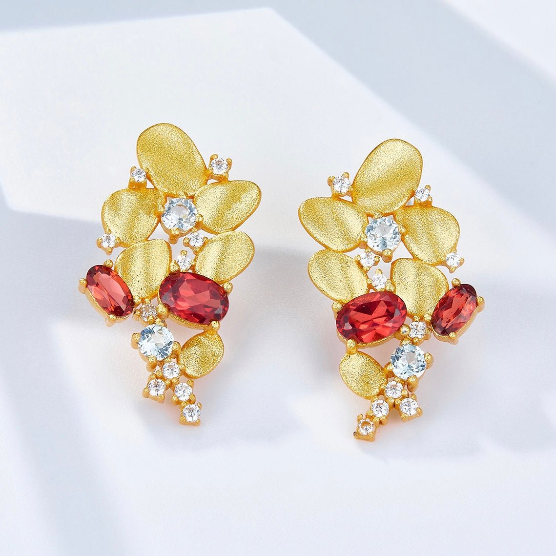 Detailed view of Opéra de Feu gold vermeil cascade earrings resting on a white surface with subtle lighting.
