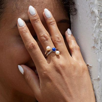 Close-up lifestyle portrait of a model's hand wearing the Awakened Time Pearl Cosmos luxury ring, highlighting its natural deep blue lapis lazuli and dual freshwater pearls set in 18ct white gold vermeil.