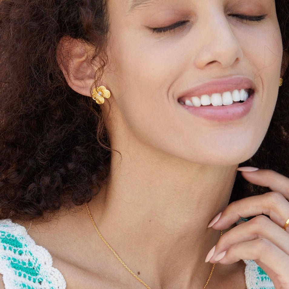 Model glowing with quiet contentment while wearing gold petal pearl stud earrings and a gold pendant necklace.