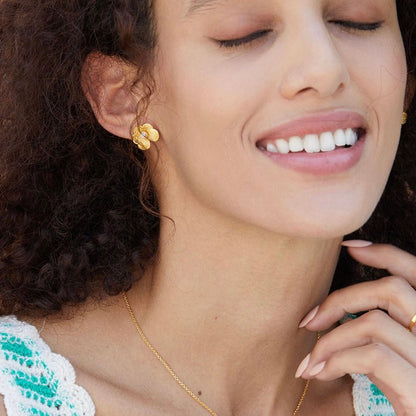 Model glowing with quiet contentment while wearing gold petal pearl stud earrings and a gold pendant necklace.