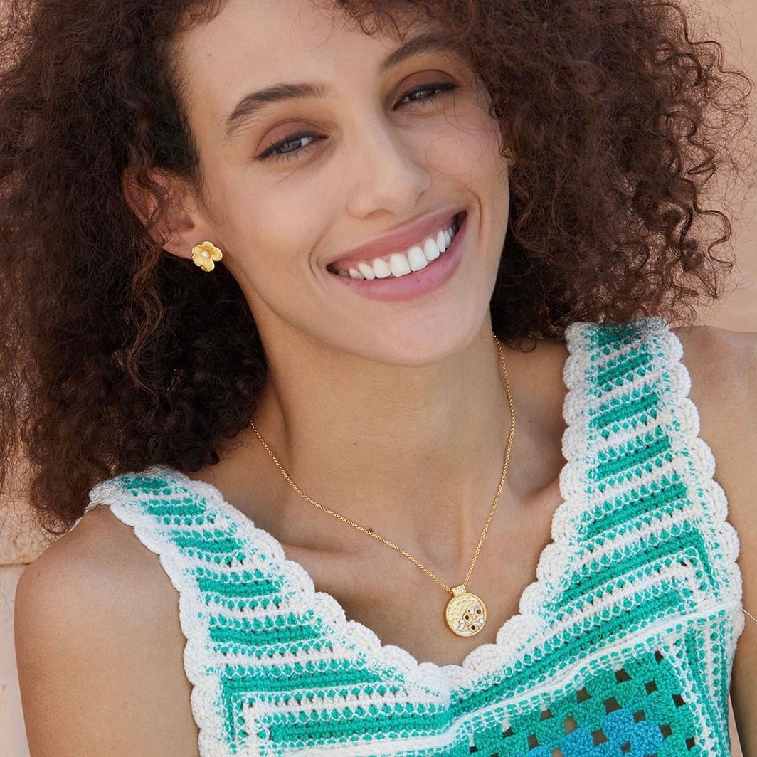 Model smiling in a green crochet top wearing the gold petal pearl stud earrings.