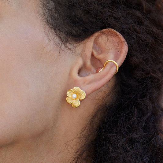 Close-up side view of a model wearing the gold petal pearl stud earring paired with a gold ear cuff.