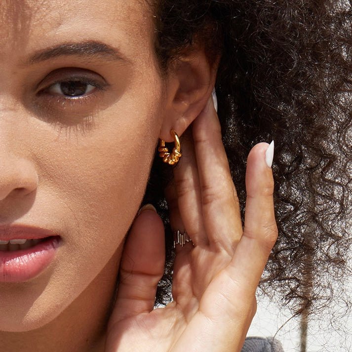 Close-up of a model wearing the Roma Twist Hoop Earrings in 18k gold vermeil.