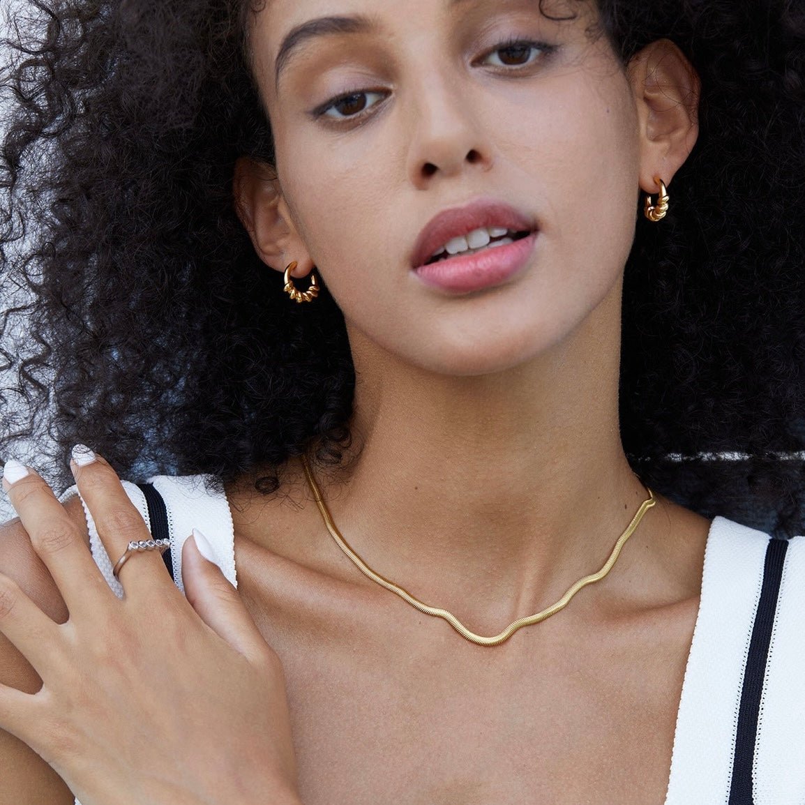 Model wearing Roma Twist gold vermeil hoop earrings styled with a gold chain necklace.